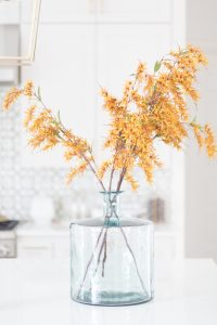 Loveliest Looks of Fall Home Tour Beautiful Fall Home Decor and Fall Fashion Ideas close up photo of yellow faux fall stems in a green vase sitting on a large quartzite waterfall kitchen countertop