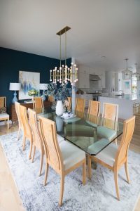 Loveliest Looks of Fall Home Tour Beautiful Fall Home Decor and Fall Fashion Ideas large white quartzite waterfall kitchen island with six gold barstools and a large green vase with yellow faux fall stems sitting on top of the countertop and gold kitchen lanterns hanging above the countertop then white kitchen cabinets with ann sacks patterned backsplash and gold hardware on the cabinets looking into a dark green dining room with a sputnik chandelier and burl wood dining room chairs