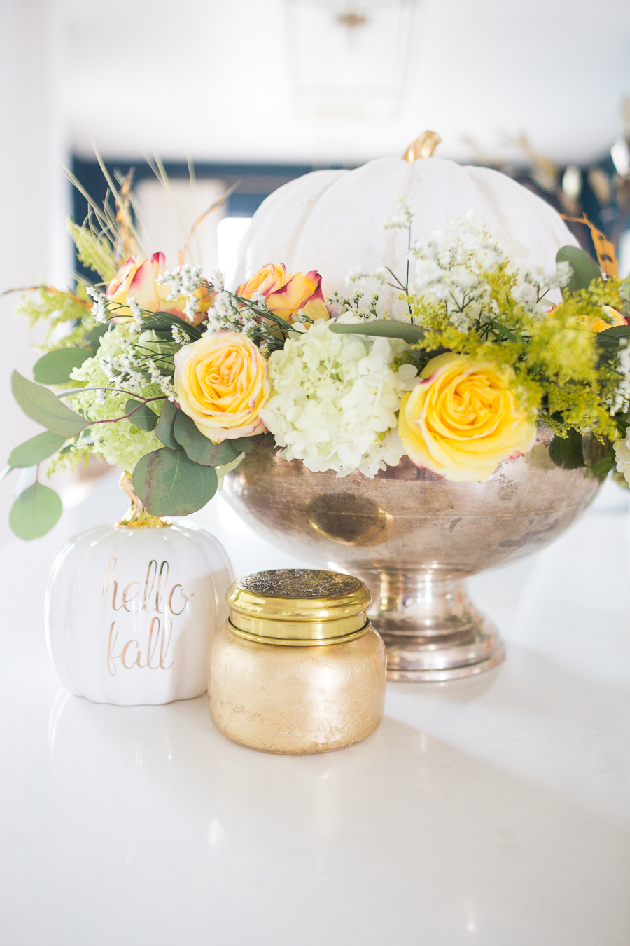 DIY Silver Urn Pumpkin Centerpiece for Fall hydrangeas and eucalyptus and roses inside of a silver urn with a ceramic pumpkin for a Thanksgiving centerpiece sitting beside a fall Anthropologie candle and hello fall pumpkin