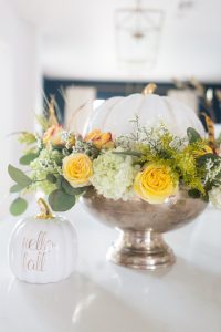 DIY Silver Urn Pumpkin Centerpiece for Fall silver urn with roses hydrangeas and eucalyptus with a ceramic pumpkin in the center sitting beside a hello fall pumpkin