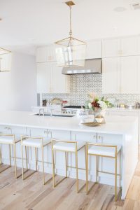 Simple Ways to Decorate for the Holidays from West Elm large wood tray faceted silver vase with hydrangeas and fall flower arrangement scented candle quartz waterfall countertops with gold bar stools copper chunky knit blanket and leopard pillows