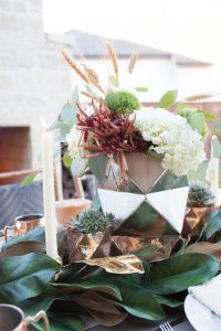 Simple Ways to Decorate for the Holidays from West Elm outdoor Friendsgiving and thanksgiving tablescape magnolia garland with gold candlesticks and a rock outdoor fireplace and copper votive candles hay bail with a chunky knit throw and copper velvet pillows