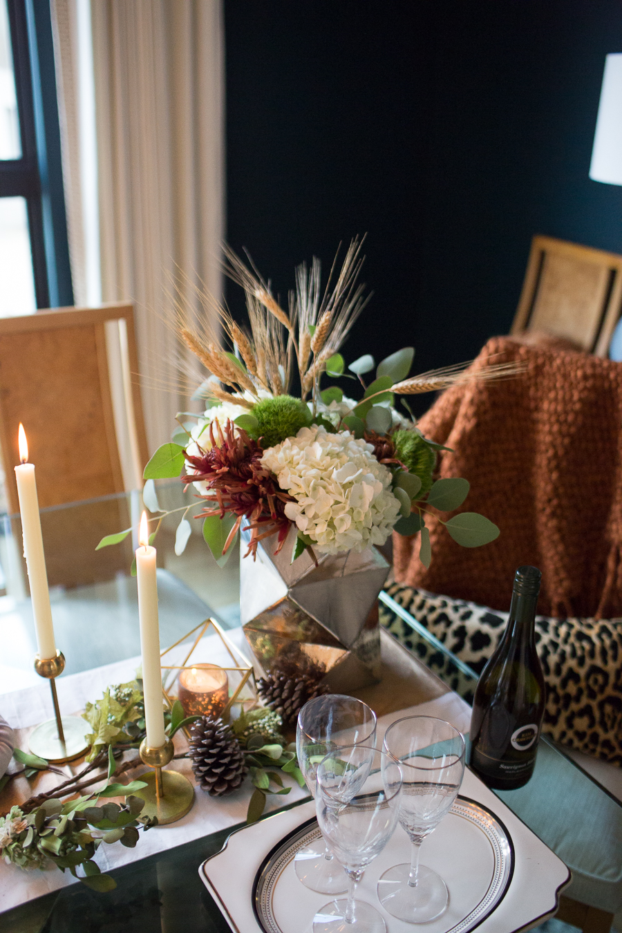 Simple Ways to Decorate for the Holidays from West Elm dark green painted dining room with glass and gold marble dining room table and burl wood chairs with a holiday tablescape with gold candlesticks and a large silver faceted vase with fresh flowers