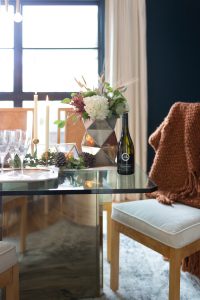Simple Ways to Decorate for the Holidays from West Elm dark green painted dining room with glass and gold marble dining room table and burl wood chairs with a holiday tablescape with gold candlesticks and a large silver faceted vase with fresh flowers