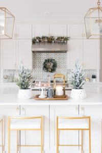 Budget Friendly Holiday Decor from Walmart white quartz waterfall island with gold bar stools and gold lanterns and a wood tray with a gold lantern and flocked Christmas trees in a polka dot vase