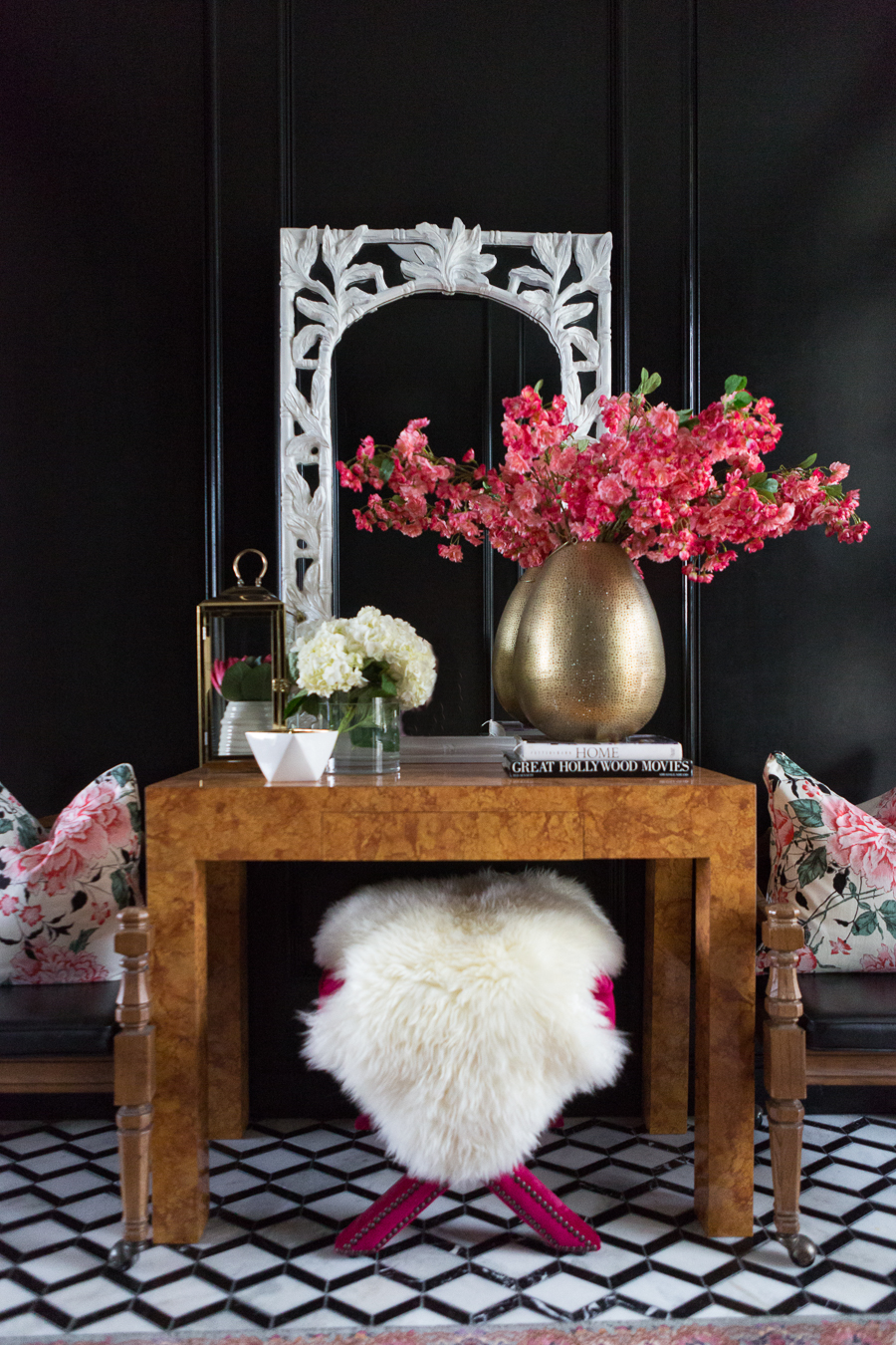 entry way table with gold vase, flowers, flower pillows and a black accented wall