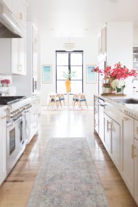 5 Tips to Decorate Your Home with Drew Barrymore Flower Home white quartz waterfall kitchen island with gold bar stools and ann sacks patterned honeycomb backsplash with gold kitchen lanterns and pink flowers styled in a kitchen