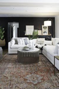 CC and Mike Kane Project Remodel Reveal white L shaped sectional on a terracotta loren rug from CC and Mike THE SHOP round coffee table black accent wall with wood art ledge