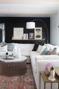 CC and Mike Kane Project Remodel Reveal white L shaped sectional on a terracotta loren rug from CC and Mike THE SHOP round coffee table black accent wall with wood art ledge