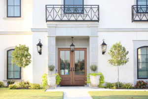 CC and Mike Frisco I Project Reveal-2 white European stucco exterior with cast stone around wooden door and topiary planters