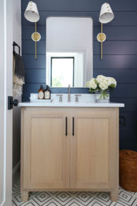 CC and Mike Frisco I Project Reveal navy shiplap wall with white oak vanity in a bathroom with silver mirror and brass and white sconces black hardware