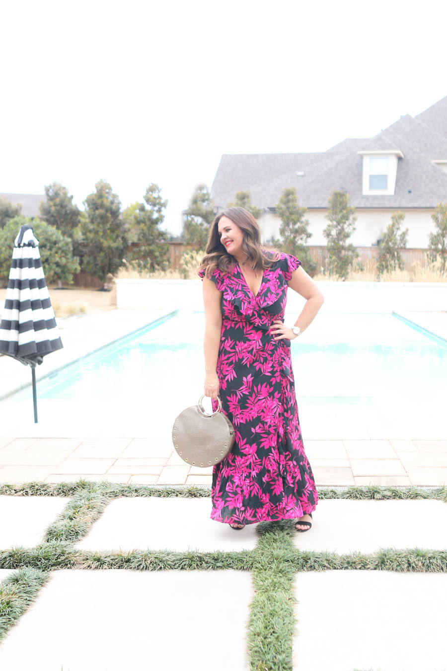 15 Must Have Walmart Fashion Items for Spring Carissa Miller standing by a rectangular pool with hot tub and black and white umbrella in a black and pink palm print wrap dress by Sofia Vergara Walmart
